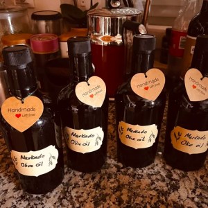 Four dark bottles of handmade olive oil with heart tags on a kitchen counter.