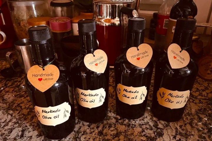 Four dark bottles of handmade olive oil with heart tags on a kitchen counter.