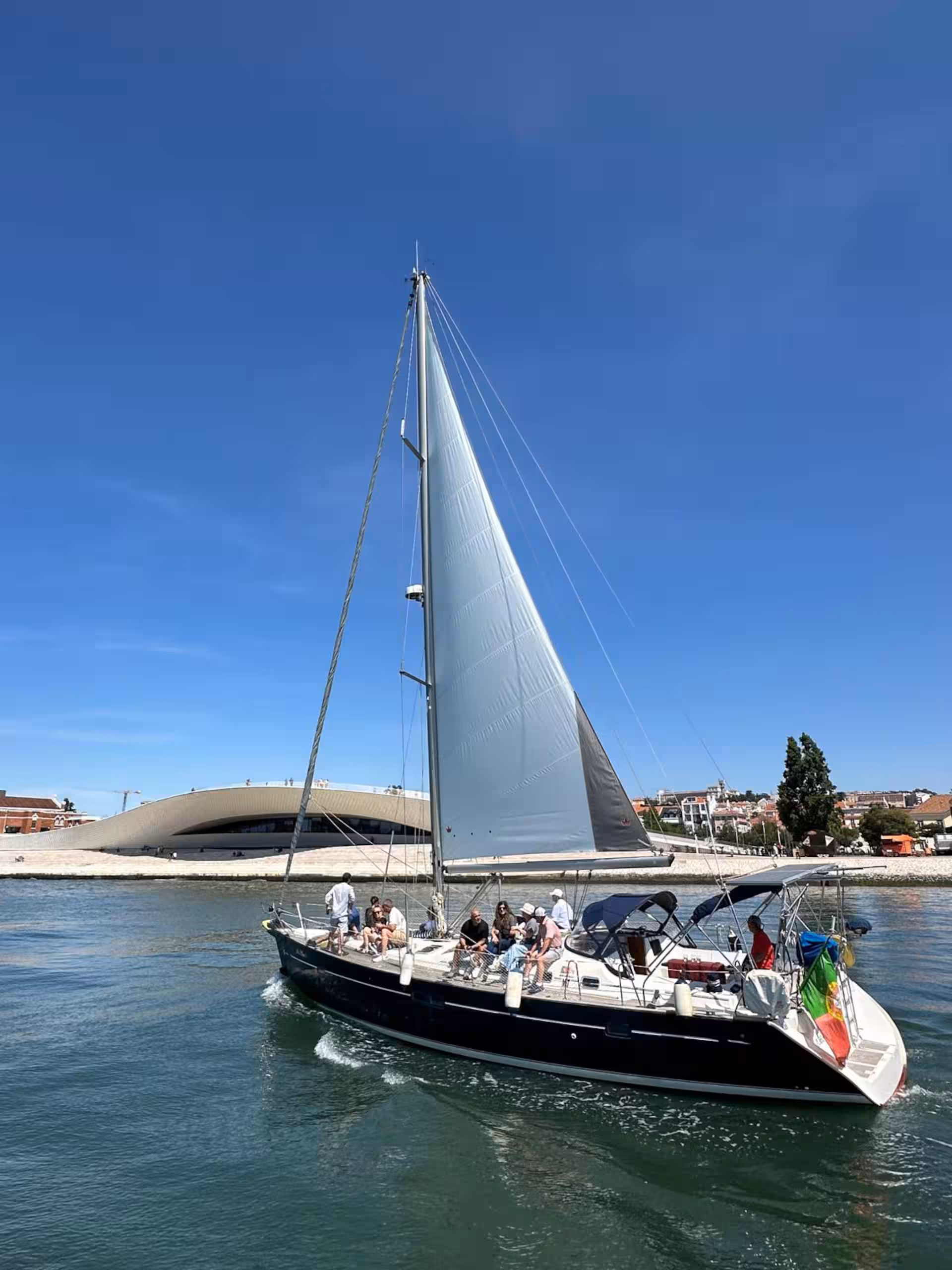 Sailboat with people on a sunny day near the shore.