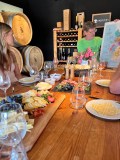 People at a wine tasting with cheese platter and wine barrels.