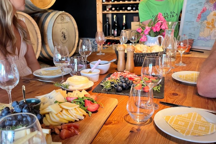 People at a wine tasting with cheese platter and wine barrels.