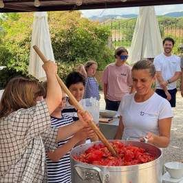 Group of people stirring a pot of chopped tomatoes outdoors.