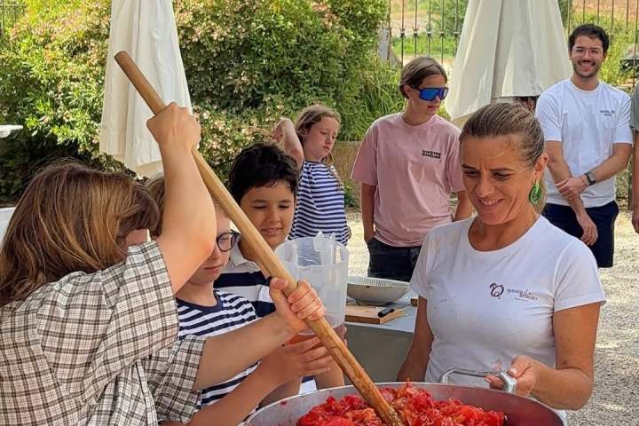 Group of people stirring a pot of chopped tomatoes outdoors.
