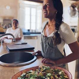 Two women in a kitchen with a large salad on the counter.
