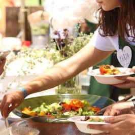 People serving salad from a large bowl at an outdoor event.