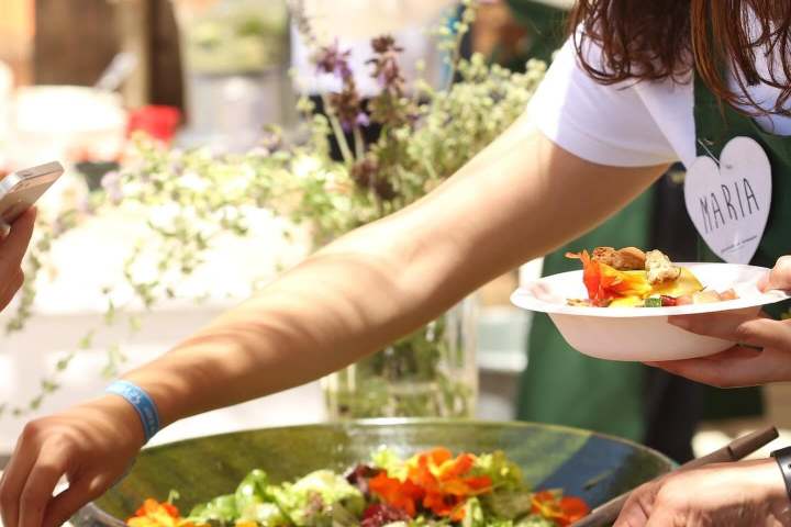 People serving salad from a large bowl at an outdoor event.
