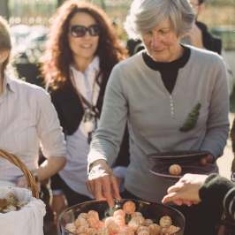 Group of people selecting oranges from a bowl at an outdoor event.