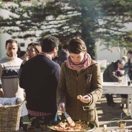 People at an outdoor gathering with a woman serving food from a large bowl.