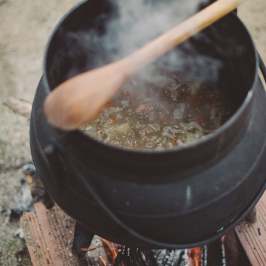 Black pot over fire with wooden spoon stirring stew.