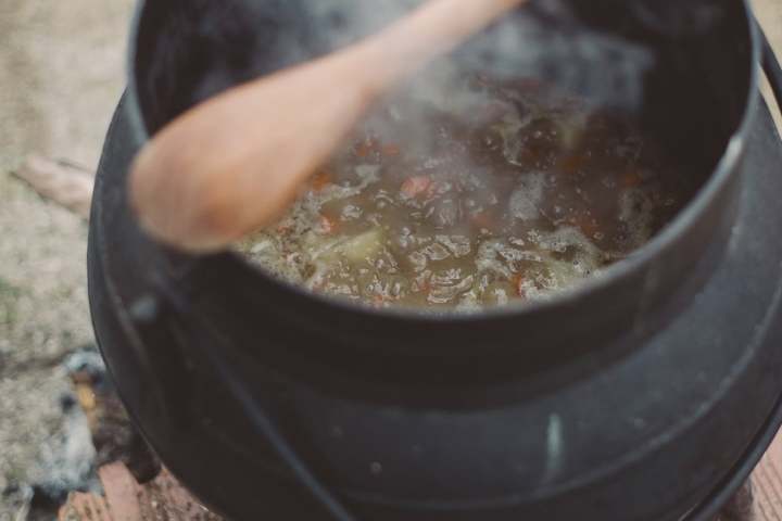 Black pot over fire with wooden spoon stirring stew.
