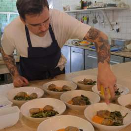 Chef plating dishes with vegetables in a kitchen setting.