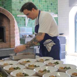 Chef plating dishes in a kitchen near a brick oven.