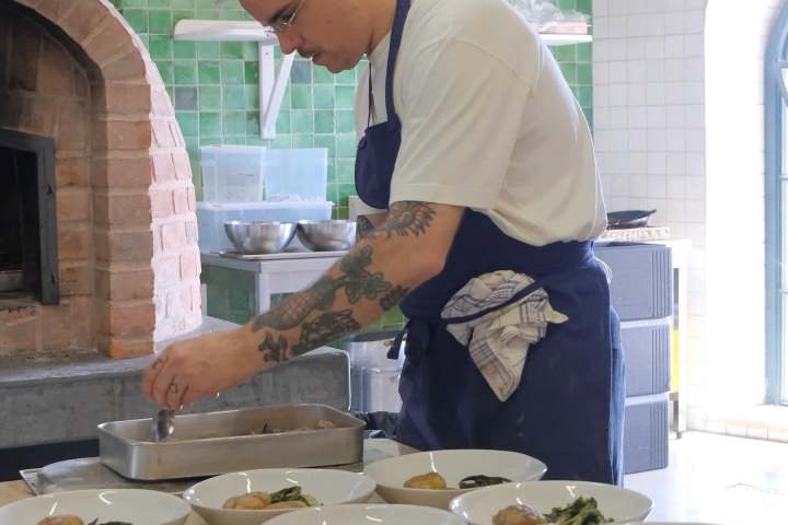 Chef plating dishes in a kitchen near a brick oven.