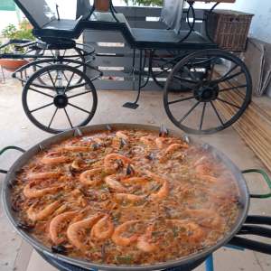 Large pan of seafood paella cooking outdoors next to a parked carriage.