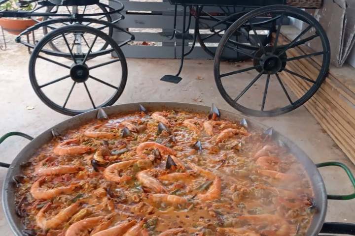Large pan of seafood paella cooking outdoors next to a parked carriage.