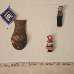 Decorative wall items include dolls, a woven ornament, a calendar, and a wood-hanging on a tiled background.
