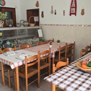 Cozy restaurant interior with wooden chairs, tablecloths, and wall decor.
