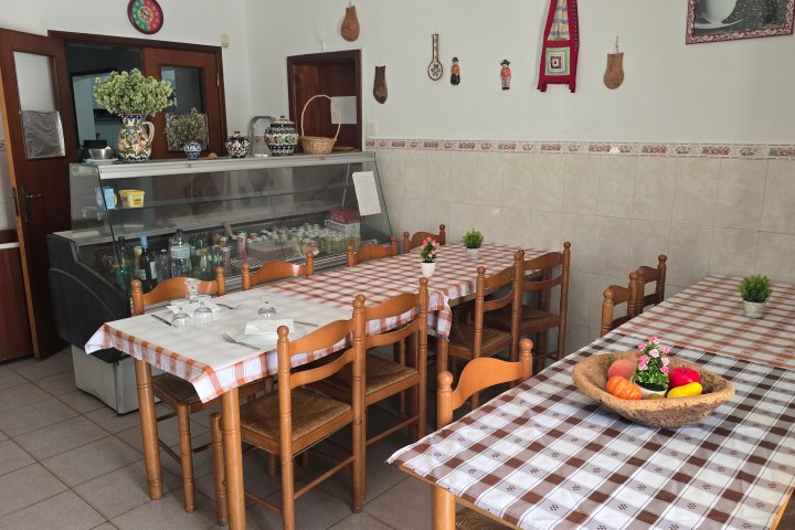 Cozy restaurant interior with wooden chairs, tablecloths, and wall decor.