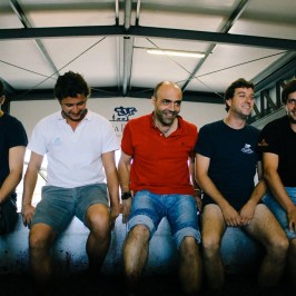 Five men sitting on a concrete ledge, wearing casual summer clothes.