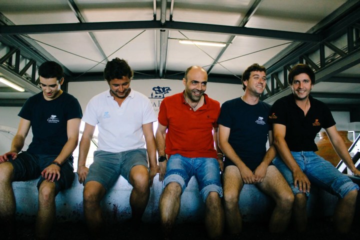 Five men sitting on a concrete ledge, wearing casual summer clothes.