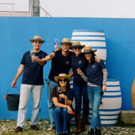 Five people in straw hats holding drinks, posing by striped barrels.
