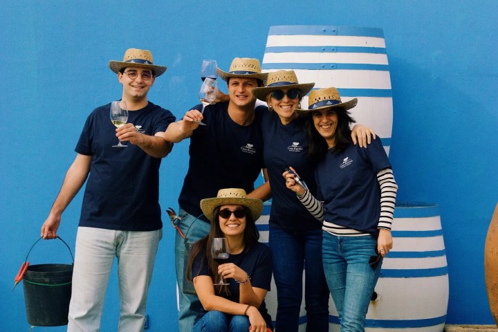 Five people in straw hats holding drinks, posing by striped barrels.
