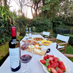Outdoor table with wine, strawberries, and various snacks in a garden setting.