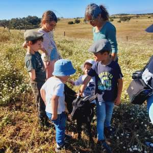 Group of children and a woman petting a black goat in a field.