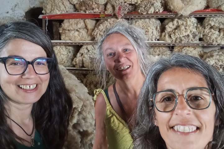 Three women smiling in front of wool rolls on racks.