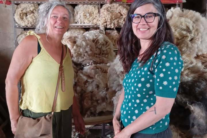 Two women standing in front of shelves filled with wool fleeces.