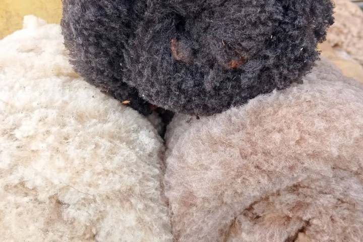 Three rolls of wool in black, cream, and brown on a surface.